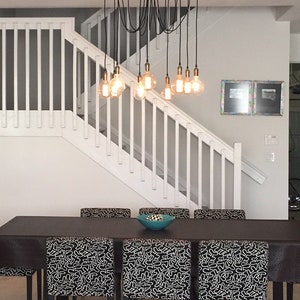 May include: A dining room with a black table and chairs. The chairs have black and white patterned fabric. A chandelier with multiple light bulbs hangs above the table.