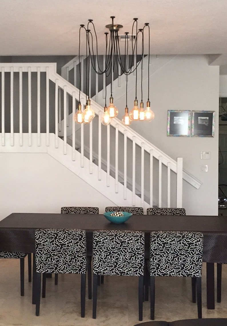 May include: A dining room with a black table and chairs. The chairs have black and white patterned fabric. A chandelier with multiple light bulbs hangs above the table.