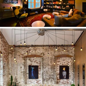 May include: Two rooms with exposed brick walls and a unique lighting fixture made of multiple Edison bulbs hanging from black cords. The first room is a living room with a bookshelf, a couch, and a chair. The second room is a dining room with a long wooden table and chairs.