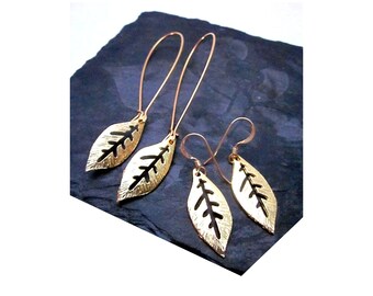 May include: Two pairs of gold-coloured leaf earrings. One pair has long, curved ear wires, the other shorter, hook-style closures. The leaf design has a cut-out pattern, revealing the dark background.