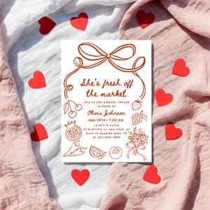 May include: A white bridal shower invitation with red text and illustrations of fruits and vegetables. The text reads "She's fresh off the market" and includes the bride's name, date, time, and location.