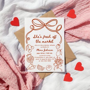 May include: A white bridal shower invitation with a red bow and the text "She's fresh off the market". The invitation includes details about the event, including the date, time, location, and RSVP information.