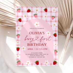 May include: Pink and white gingham patterned invitation with red strawberries and white flowers. The text reads "Join us to celebrate Olivia's berry & first birthday, April 25, 12-4 PM, at Olivia's home, 123 Rainbow Street, New York, NY, RSVP by March 15th, to Mom at +123 456 789".