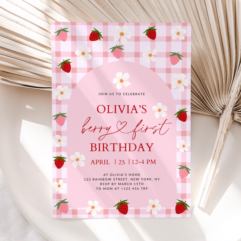 May include: Pink and white gingham patterned invitation with red strawberries and white flowers. The text reads "Join us to celebrate Olivia's berry & first birthday, April 25, 12-4 PM, at Olivia's home, 123 Rainbow Street, New York, NY, RSVP by March 15th, to Mom at +123 456 789".