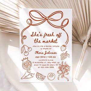 May include: A red and white bridal shower invitation with a hand-drawn illustration of a bow, cherries, a strawberry, grapes, a pomegranate, peppers, an orange, and a bouquet of flowers. The text reads "She's fresh off the market" and includes the bride's name, date, time, and location.