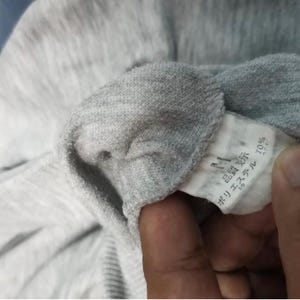 May include: Close-up of a gray fabric garment with a tag. The tag has Japanese text and indicates 70% polyester. The fabric appears to be a knit material.