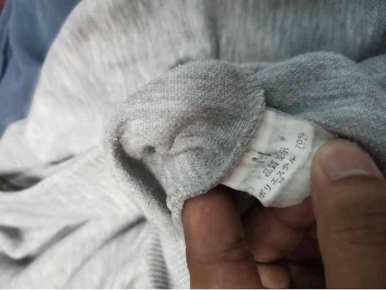 May include: Close-up of a gray fabric garment with a tag. The tag has Japanese text and indicates 70% polyester. The fabric appears to be a knit material.