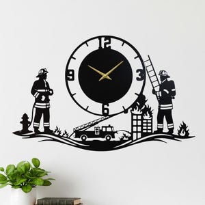 Puede incluir: Reloj de pared de metal negro con temática de bombero. El reloj tiene una esfera circular con manecillas doradas y un diseño de silueta de bomberos, un camión de bomberos y un edificio en llamas. El reloj está montado en una pared blanca.
