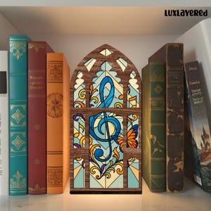 May include: A wooden, stained-glass style light with a musical note design. The light is in the shape of a church window, with a brown frame and colorful glass. The musical note is blue, with orange and yellow accents. The light is on a shelf with books.