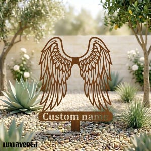 Può includere: Un paletto da giardino in metallo marrone con ali d'angelo con dettagli di piume intricati. Il paletto include il testo "Custom name" ed è progettato per l'uso all'aperto. Le ali sono un elemento decorativo per giardini e spazi commemorativi.