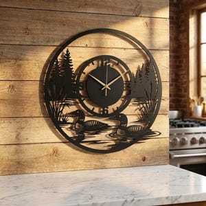 Puede incluir: Un reloj de pared circular de metal negro con un diseño de silueta de dos colimbos nadando en el agua, rodeados de espadañas y pinos. La esfera central tiene un fondo negro sólido con manecillas de hora y minuto de color dorado.