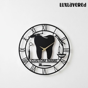 May include: Black metal wall clock with a dental theme. The clock features a large tooth in the center, surrounded by dental tools and Roman numerals. The clock hands are gold, and the text "CUSTOM NAME" is at the bottom.