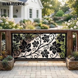 May include: A rectangular black metal privacy screen featuring a laser-cut design of maple leaves and swirling vine patterns. The panel is mounted within a wooden frame, positioned between two stone planters on a paved patio area.
