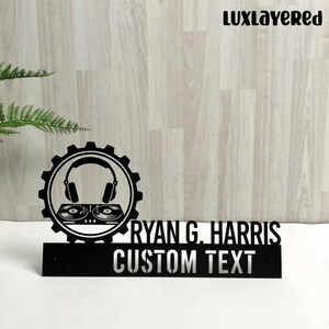Puede incluir: Letrero de escritorio de metal negro con un gráfico de configuración de DJ, que incluye auriculares y tocadiscos dentro de un engranaje. El letrero muestra el nombre "RYAN G. HARRIS" y las palabras "CUSTOM TEXT".
