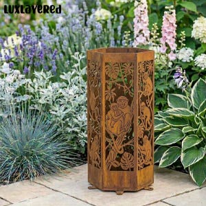 May include: A tall, hexagonal, rusty brown metal garden lantern. The lantern features cut-out designs of monkeys and tropical foliage. The lantern is placed on a stone patio, surrounded by lush greenery and flowers.