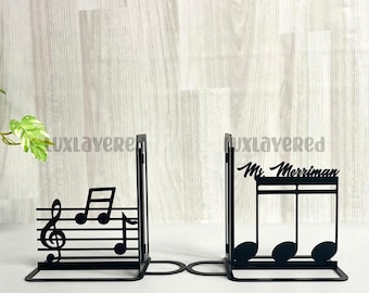 Puede incluir: Par de sujetalibros de metal negro con diseños de notas musicales. Un sujetalibros tiene el nombre "Mr. Merriman". Estos sujetalibros están diseñados para mantener los libros en posición vertical y añadir un toque decorativo a una estantería.