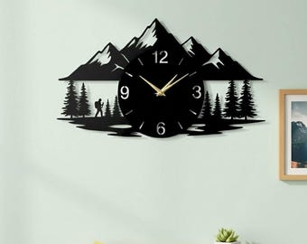 May include: Black mountain-themed wall clock with a circular clock face. The clock features gold-colored hands and numbers, with a mountain range silhouette above and trees and a hiker below. The brand name "LUXLAYERED" is at the top left.