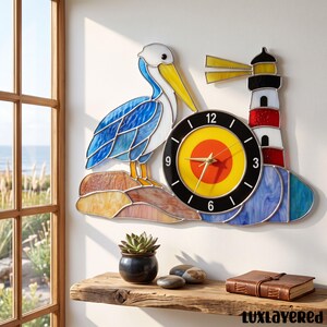 May include: A stained glass wall clock featuring a blue and white pelican standing on a tan rock next to a red, white, and black lighthouse. The clock face is yellow and orange with a black border, white numbers, and gold-colored hands.
