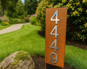 Puede incluir: Un letrero de dirección rectangular de metal envejecido con los números 4449 en acabado plateado. El letrero está montado sobre dos estacas de metal y está colocado en un jardín con césped verde, una piedra y un sendero.