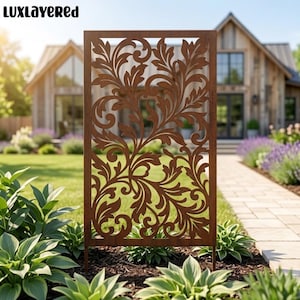 May include: A rectangular metal garden screen featuring a rust-colored finish and an intricate laser-cut pattern of swirling acanthus leaves and vines. The panel is positioned vertically in a garden bed with green hosta plants at the base.