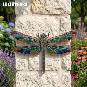 May include: A dragonfly wall decoration featuring iridescent stained glass wings in shades of blue, green, and gold, framed by a copper-toned metal outline. The insect has a segmented body with matching blue and green glass accents.