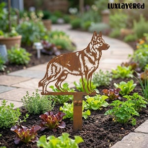 May include: A rusty brown metal garden stake featuring a German Shepherd dog silhouette. The dog is standing, with detailed cut-out fur patterns. The stake is in a garden bed with green and red plants, and the text "LUXLAYERED" is in the top right corner.
