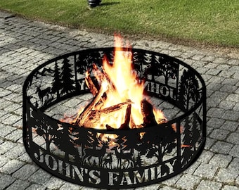 Könnte beinhalten: Eine schwarze Metall-Feuerstelle mit einem ausgeschnittenen Design einer Waldszene. Die Feuerstelle hat eine kreisförmige Form und zeigt Hirsche, Bäume und den Text "JOHN'S FAMILY". Die Feuerstelle ist mit brennendem Holz und Flammen gefüllt.