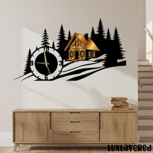 May include: A black and gold metal wall clock featuring a cabin scene with pine trees and a clock face. The clock hands are gold. The cabin has a gold roof and is set against a white wall. The clock is a decorative item.