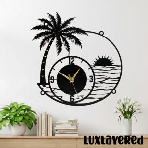 Könnte beinhalten: Schwarze Metall-Wanduhr mit Palmen-, Sonnen- und Ozean-Design. Das Zifferblatt ist schwarz mit goldenen Zeigern und weißen Ziffern. Der Text "LUXLAYERED" befindet sich unten.
