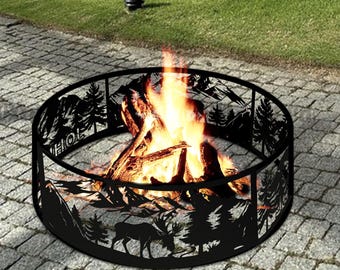 Könnte beinhalten: Ein schwarzer, kreisförmiger Feuerkorb mit einem dekorativen Berg- und Wald-Silhouette-Design. Der Feuerkorb enthält ein brennendes Feuer mit orangefarbenen und gelben Flammen. Das Wort "HOE" ist auf der Seite des Feuerkorbs zu sehen.