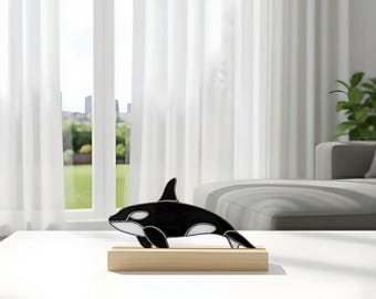 May include: A black and white orca whale figurine on a rectangular wooden base. The orca has white markings and is displayed on a white table in front of a window with white curtains. The word "LUXLAYERED" is at the bottom.