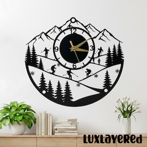 May include: Black metal wall clock with a ski scene design. The clock features a circular face with gold hands, surrounded by a silhouette of mountains, skiers, and trees. The text "LUXLAYERED" is at the bottom.