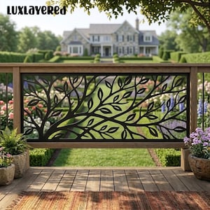May include: A black metal railing panel featuring a decorative laser-cut tree branch and leaf pattern. The rectangular panel is framed by wooden posts and rails, positioned on a wooden deck with potted plants on either side. Text reads LUXLAYERED.