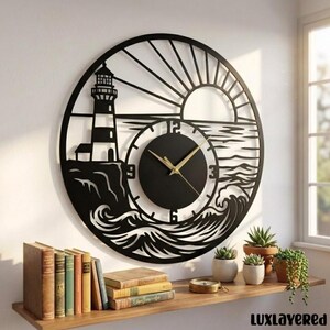 May include: A circular black metal wall clock featuring a laser-cut design of a lighthouse on a cliff, ocean waves, and a rising sun. The clock face is centered with gold-colored hands and numerical markers for 3, 6, 9, and 12 o'clock.