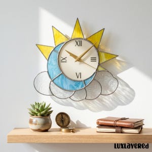 May include: A decorative wall clock featuring a sun, moon, and cloud design. The clock face is cream-colored with Roman numerals and gold-colored hands. The sun is yellow, the moon is blue, and the clouds are white. The clock is mounted on a white wall.