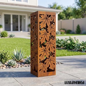 May include: A tall, rectangular, rust-coloured metal garden pillar featuring a laser-cut pattern of maple leaves on all visible sides. The structure has a weathered, oxidised finish and stands upright on a flat, paved surface outdoors.