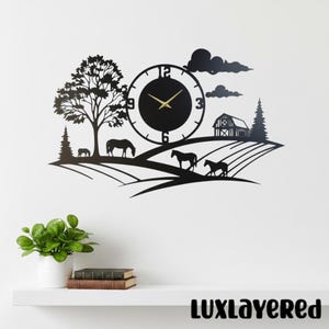 May include: A black metal wall clock featuring a rural landscape silhouette with horses, a large tree, a barn, and clouds. The circular clock face has gold-colored hands and numbers at the 3, 6, 9, and 12 positions, integrated into the scene.