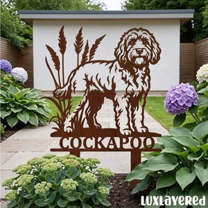 Può includere: Un picchetto da giardino in metallo color ruggine con la sagoma ritagliata di un cane Cockapoo tra steli d'erba alta. La parola COCKAPOO è ritagliata in lettere maiuscole lungo la barra orizzontale alla base dell'ornamento in metallo.