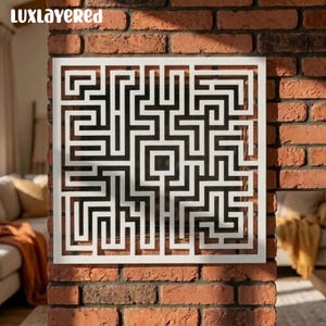 Puede incluir: Una pieza de arte mural cuadrada de color blanco que presenta un complejo patrón de laberinto geométrico con caminos interconectados y una abertura cuadrada central. El diseño consta de líneas gruesas y uniformes en una superficie plana.