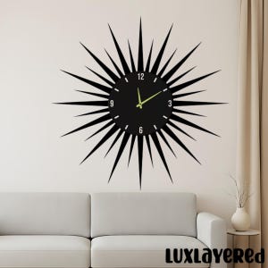 May include: A black sunburst wall clock featuring a circular face with white numerals at the 3, 6, 9, and 12 o'clock positions. The clock has long, pointed black rays extending outward and two light-colored hands indicating the time.