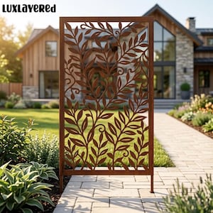 May include: A rectangular metal garden screen with a rust-colored finish featuring a laser-cut pattern of climbing vines and leaves. The vertical panel is supported by two thin legs and stands on a paved walkway in front of a residential home.