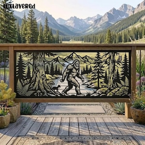 May include: A black metal decorative panel featuring a laser-cut silhouette of a Bigfoot walking through a forest with mountains in the background. The design includes trees, a small fox, mushrooms, and an owl. The text Luxlayered is in the corner.