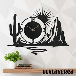 May include: Black metal wall clock featuring a desert landscape design with a cactus, mountains, and sun. The clock face is round with black hands and numbers. The brand name "LUXLAYERED" is at the bottom.