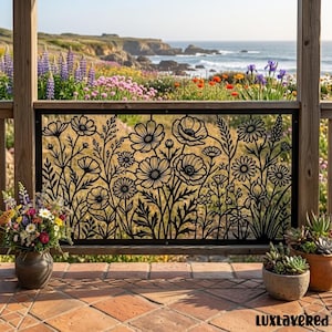 May include: A black metal decorative panel featuring a laser-cut floral design with various wildflowers and stems. The rectangular panel is framed and installed as a railing insert, showcasing intricate botanical silhouettes against a coastal view.