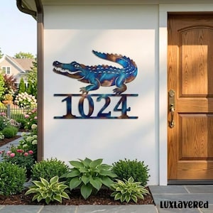 Könnte beinhalten: Ein Hausnummernschild aus Metall mit den Ziffern 1024 in fetter Schrift, gekrönt von einer stilisierten Alligatorfigur. Das Schild hat ein blau-kupferfarbenes Finish und ist an einer weißen Außenwand neben einer Holztür montiert.
