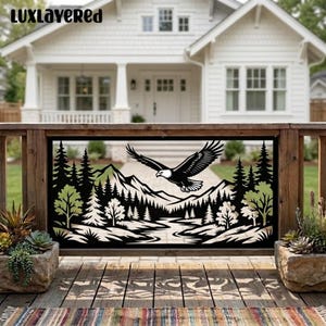 May include: A black metal decorative panel featuring a laser-cut design of a bald eagle in flight above a mountain range, a forest of pine trees, and a winding river. The text LUXLAYERED is visible in the top left corner of the rectangular frame.