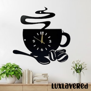 Könnte beinhalten: Schwarze Wanduhr in Form einer Kaffeetasse mit Löffel und Kaffeebohnen. Die Uhr hat goldene Zeiger und weiße Zahlen. Das Wort "LUXLAYERED" steht unten. Die Uhr befindet sich an einer weißen Wand.
