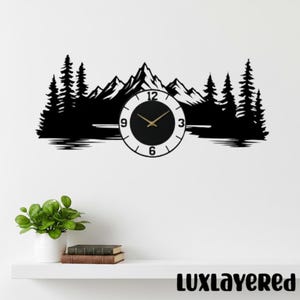 May include: A black wall clock featuring a silhouette of a mountain range and pine trees. The clock face is white with black numbers and gold hands, integrated into the center of the landscape design, creating a wide, horizontal display.