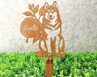 May include: A brown metal garden stake featuring a cut-out design of a dog, holding a circular sign with the name "Koda". The stake is placed in a bed of green plants. The brand name "LUXLAYERED" is in the top left corner.