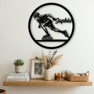 May include: Black metal wall art featuring a silhouette of a person inline skating inside a circular frame. The name "Sophia" is scripted in cursive. The artwork is mounted on a white wall above a wooden shelf with decorative items.